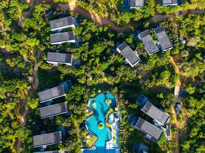 Letecký pohled na resort s bazénem a několika obdélníkovými budovami obklopenými zelenou vegetací.