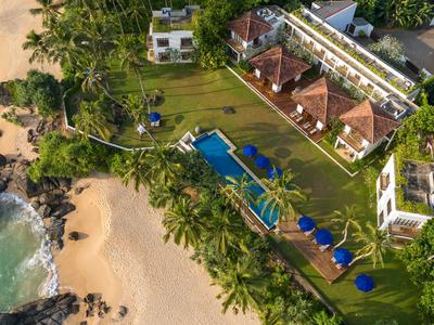 Luxuriöses Hotel mit Pool und Garten direkt am tropischen Sandstrand und Palmen.