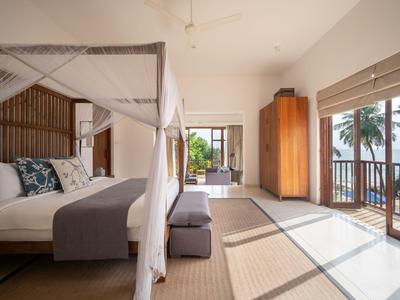 Helles Hotelzimmer mit Himmelbett, Holzmöbeln und Blick auf Palmen und Terrasse.