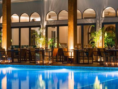 Buitenruimte van een hotel met verlicht zwembad en zitplaatsen 's nachts.