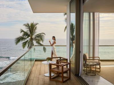 Balkon met glazen balustrade met uitzicht op zee, palmboom en persoon die van het uitzicht geniet.