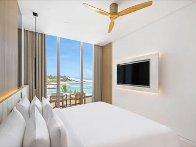 Moderne hotelkamer met tweepersoonsbed, plafondventilator en balkon met uitzicht op zee.