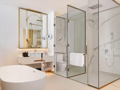 Modern hotelbadkamer met vrijstaand bad en glazen douchedeur in lichte tinten.
