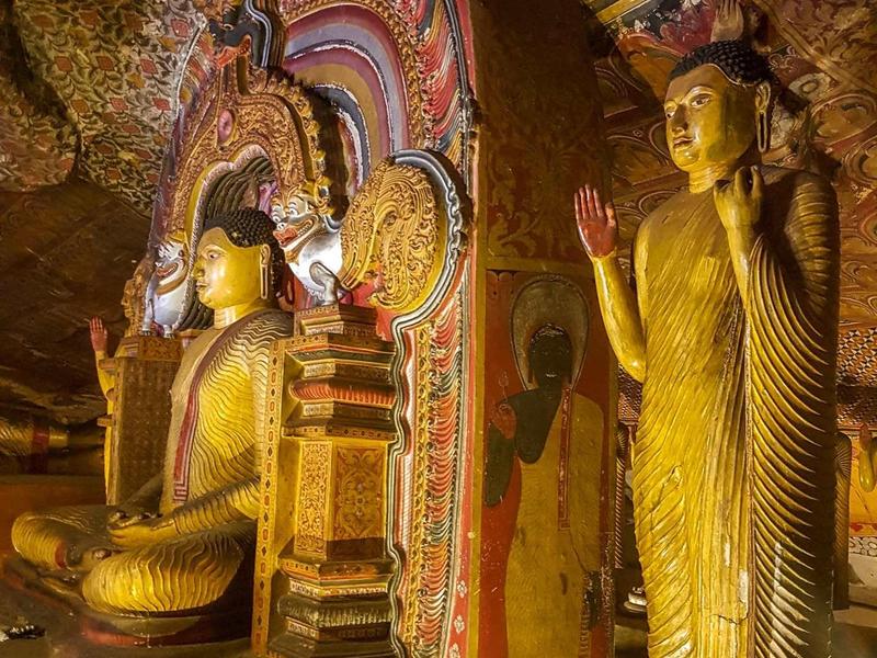 Tempel mit goldenen Buddha-Statuen vor bunt verziertem Wand- und Deckendekor.