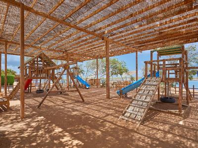 Un área de juegos sombreada con estructuras de madera y toboganes bajo un techo de paja en un jardín de hotel.