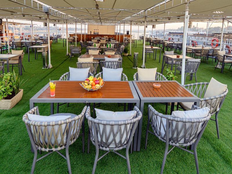Terraza de restaurante con mesas y sillas sobre césped artificial bajo techo, decoración moderna.