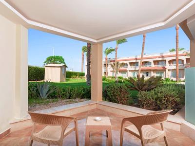 Outdoor seating area with two chairs and a table on a patio, overlooking a garden and hotel building.