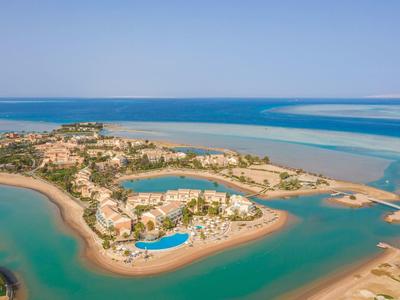 Aerial view of a coastal island with resort, pool, and clear blue sea water.