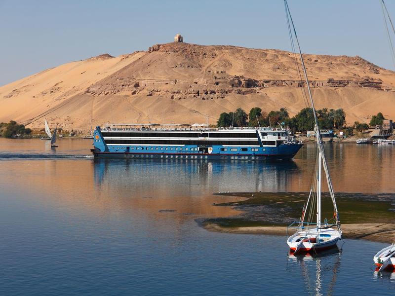 River scene with boats and a hill in the background under clear sky.