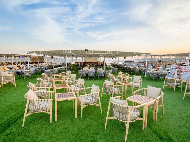 Outdoor seating area with multiple tables and chairs on green artificial grass under a large white canopy.