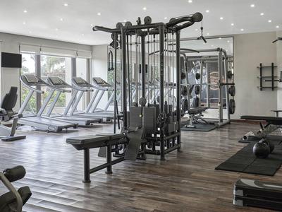 Moderner Fitnessraum mit verschiedenen Trainingsgeräten und Laufbändern, helle Fensterfront