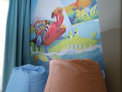 Twee zitzakken, blauw en bruin, voor een kleurrijke tropische muurschildering bij een raam met blauwe gordijnen.