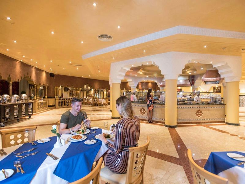 Elegant hotelrestaurant met gasten aan tafel, blauwe en witte tafeldecoratie, warme verlichting.