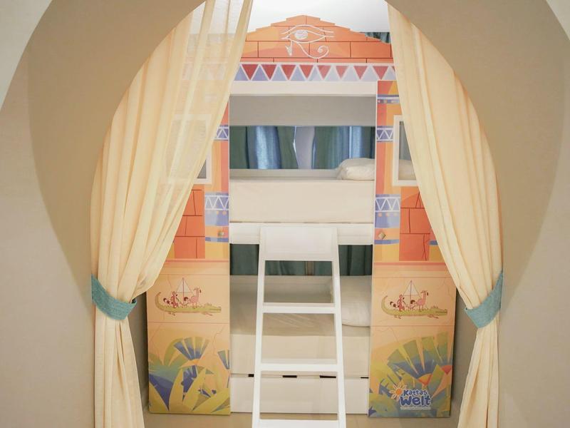 Een knusse slaaphoek met gordijnen, ladder en kleurrijke wanddecoraties.