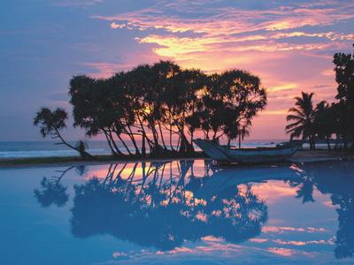 Sonnenuntergang über einem Pool mit reflektierenden Bäumen am Strand