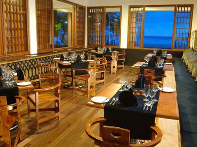 Elegantes Restaurant mit Holzmöbeln und Meerblick durch große Fenster bei Dämmerung.