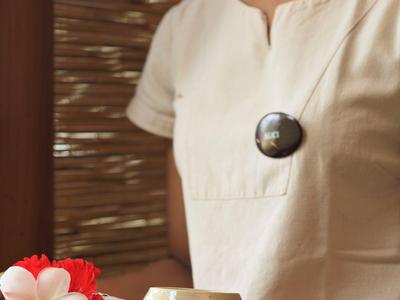 Person hält ein Tablett mit Blume und Tasse, getragen von einer in Cremefarben gekleideten Person.