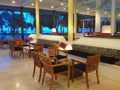 Moderner Hotel-Loungebereich mit Holztischen, Stühlen und gepolsterten Sitzbänken bei Abendlicht.