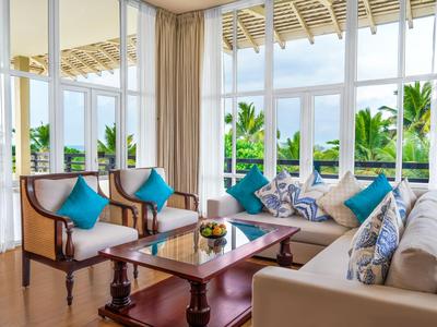 Helles Wohnzimmer mit weißen Sofas, blauen Kissen und großen Fenstern mit Blick auf tropische Pflanzen.