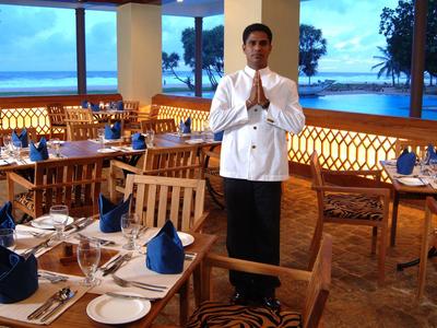 Kellner in einem elegant gedeckten Restaurant mit Blick auf das Meer bei Sonnenuntergang.