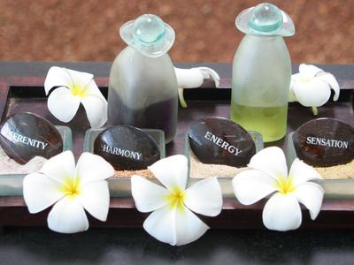 Elegantes Set mit Aromatherapieöl, Seifen und weißen Blumen auf Holztablett.