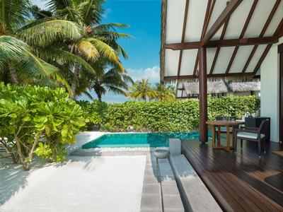 Terrasse mit Holzdeck, Pool und tropischer Vegetation unter blauem Himmel.
