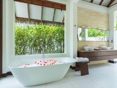 Freistehende Badewanne mit Rosenblättern, großer Spiegel und Blick auf grünen Garten.