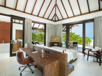 Modernes Hotelzimmer mit Holzmöbeln, Schreibtisch, Bett und Meerblick durch große Fenster.