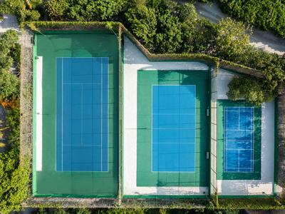 Drei Tennisplätze unterschiedlicher Größe, umgeben von Büschen und Wegen.