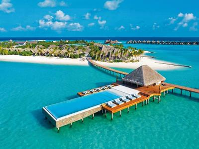 Luxuriöse Überwasservillen mit Pool auf klarem türkisfarbenem Wasser und weißem Sandstrand.