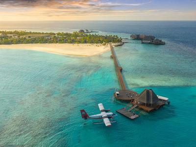 Überblick über ein Resort mit Pier und Wasserflugzeugen im türkisfarbenen Meer bei Sonnenuntergang.