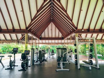 Fitnessraum mit modernen Geräten unter einem hohen, offenen Holzdach.