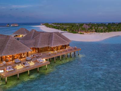 Überwasserbungalows mit Strohdächern am klaren Meer bei Sonnenuntergang