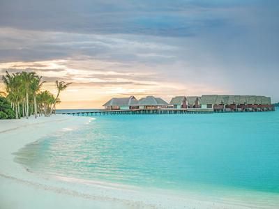 Bungalows auf Stelzen über türkisfarbenem Wasser mit weißen Sandstrand und Palmen