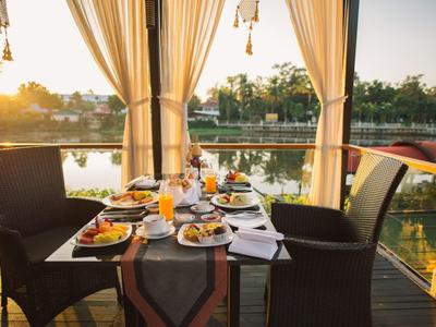 Ein gedeckter Gartentisch mit Speisen und Getränken vor einem See bei Sonnenuntergang.