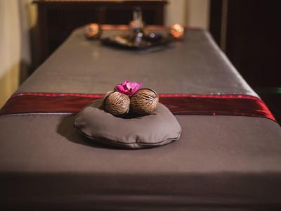 Massagebett mit dunkler Abdeckung, Nüssen und Blume als Dekoration, entspannende Atmosphäre