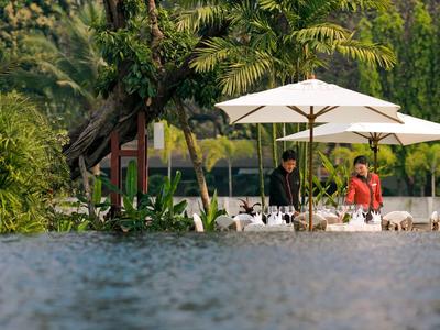 Zwei Personen neben einem Tisch unter Sonnenschirmen am Ufer mit Wasser im Vordergrund