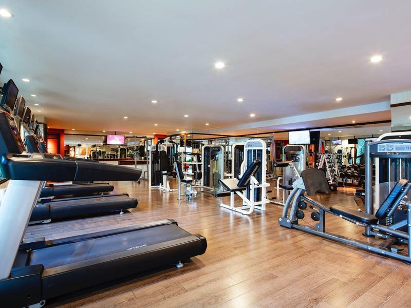 Großer Fitnessraum mit modernen Geräten und Holzfußboden in hellem Ambiente.