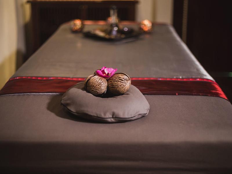 Massagebett mit dunkler Abdeckung, Nüssen und Blume als Dekoration, entspannende Atmosphäre