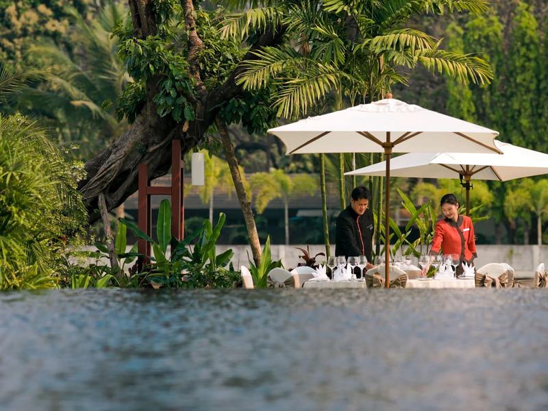 Zwei Personen neben einem Tisch unter Sonnenschirmen am Ufer mit Wasser im Vordergrund