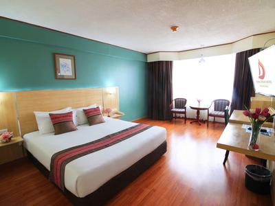 Helles Hotelzimmer mit Doppelbett, grün gestrichener Wand und großem Fenster mit Vorhängen