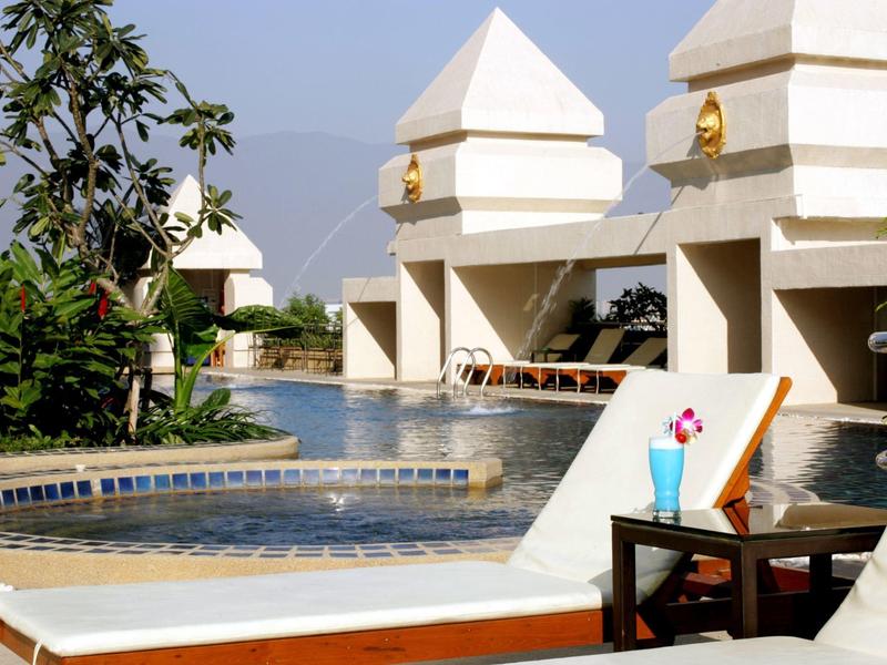 Poolbereich eines Hotels mit Liegestühlen, Pflanzen und weißen Architekturdetails.