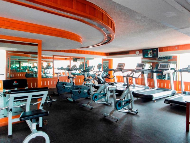 Helles Fitnessstudio mit modernen Geräten und orangen Wänden, Spiegelflächen und Fensterblick.