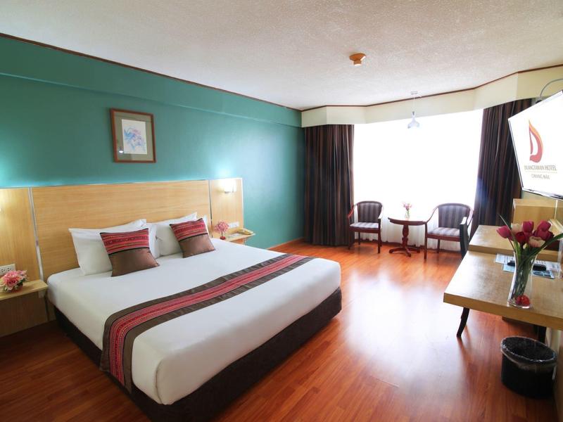 Helles Hotelzimmer mit Doppelbett, grün gestrichener Wand und großem Fenster mit Vorhängen