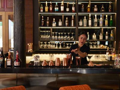 Barkeeper bereitet einen Cocktail in einer stilvollen Hotelbar mit beleuchteten Regalen vor.