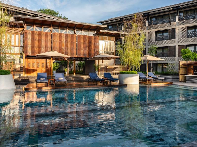 Moderner Hotelpool mit Liegestühlen und Holzgebäuden bei klarem Himmel.