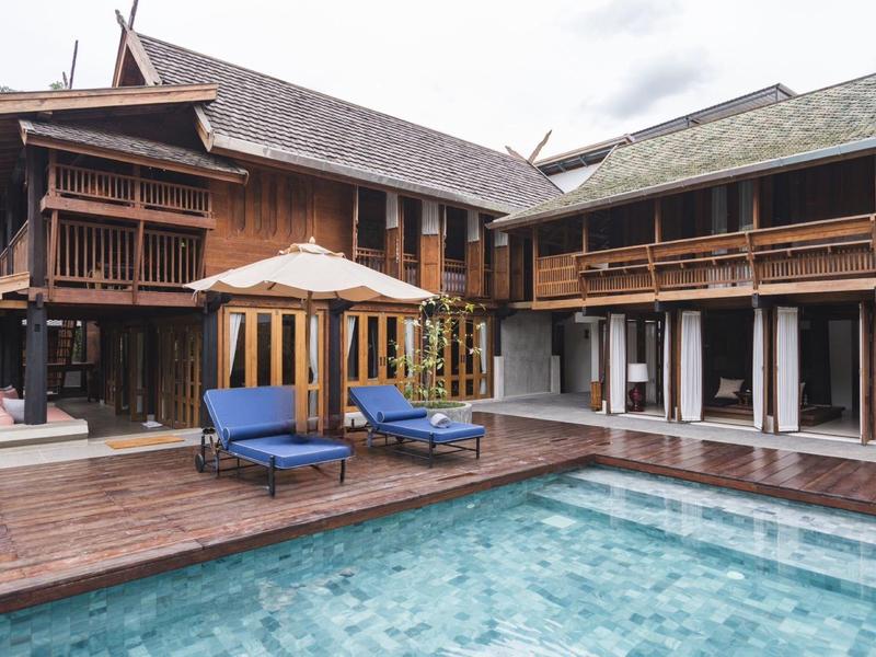 Resort mit Holzhäusern und einem Pool mit blauen Liegestühlen auf einer Holzterrasse.