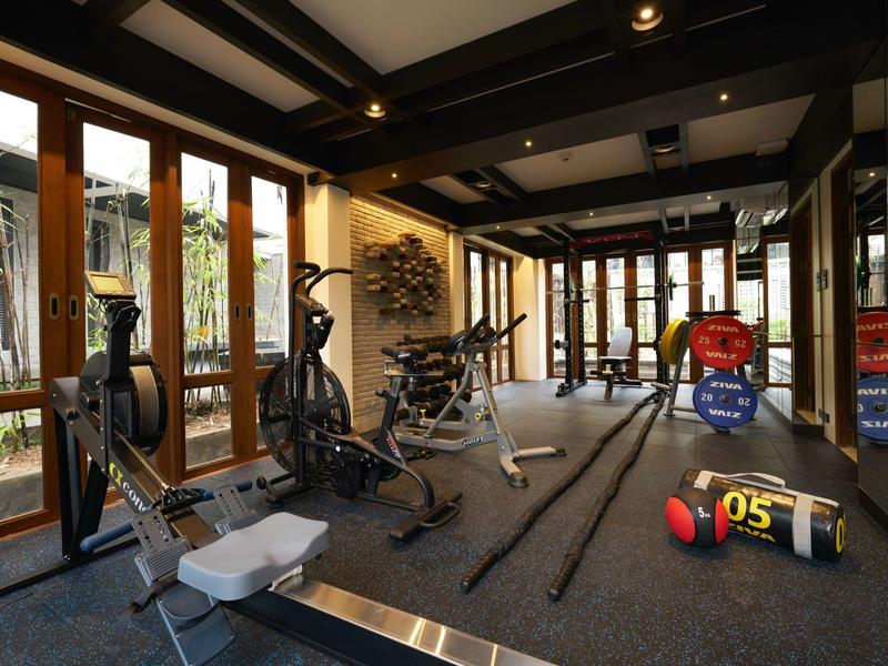 Moderner Fitnessraum mit Trainingsgeräten und großen Fenstern mit Blick auf Pflanzen.