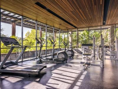 Heller Fitnessraum mit modernen Geräten und großem Fensterblick auf grüne Bäume.