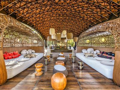 Otevřená odpočinková zóna s prohnutým dřevěným designem a polštáři v teplých tónech.